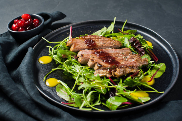 Sığır eti biftek, roka ve siyah bir tabak pazı salatası. Kızılcık sosu. Üstten Görünüm, siyah arka plan, kapat - Fotoğraf, Görsel