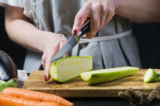 Hände Koch schneiden Zucchini auf einem hölzernen Schneidebrett. Seitenansicht, schwarzer Hintergrund, Nahaufnahme - Foto, Bild