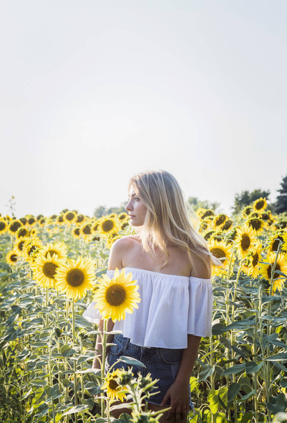 Beautiful blonde Caucasian woman standing at sunflower field. - Valokuva, kuva