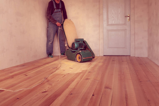 Tischler poliert Holzboden mit elektrischer Holzschleifmaschine in einem Raum - Foto, Bild