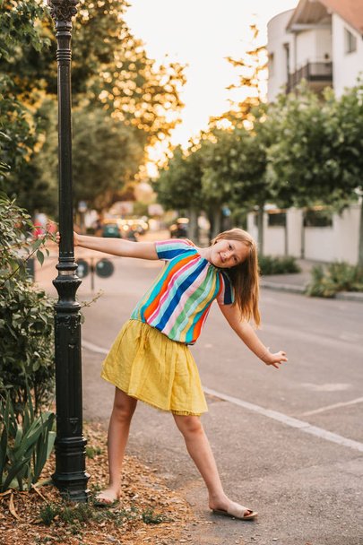 Summer portrait of pretty kid kid girl posing outdoors, wearing yellow skirt and colorful blouse - Valokuva, kuva