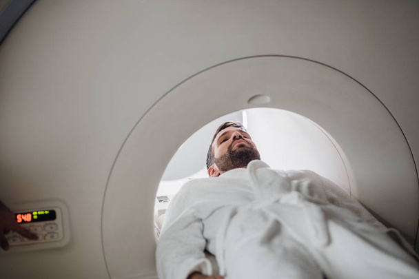 Young Caucasian man  lying on the CT scanner bed. - Photo, image