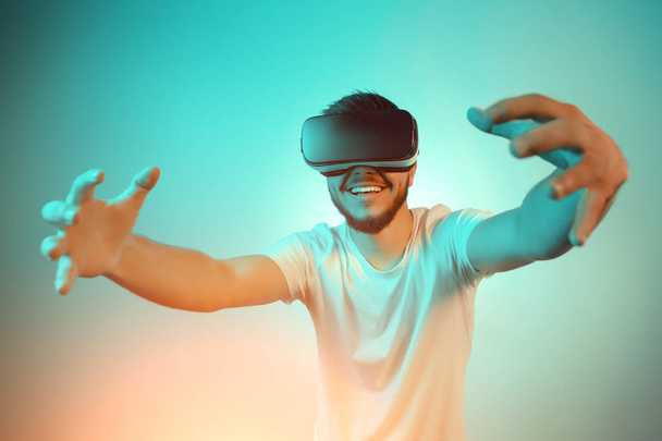 Pretty bearded man trying VR headset and exploring another world on the colorful background. Smartphone using with VR headset. - Foto, Imagen