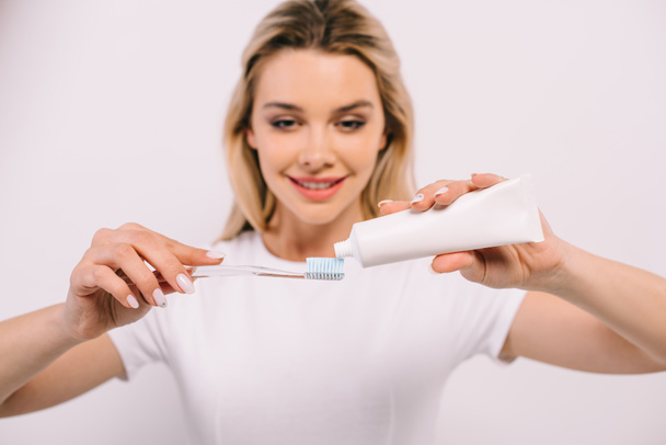 schöne lächelnde Frau, die Zahnpasta auf Zahnbürste legt, isoliert auf weiß - Foto, Bild