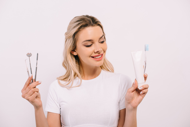 красивая улыбающаяся женщина с зубной пастой, зубной щеткой и зубными инструментами, изолированными на белом
 - Фото, изображение