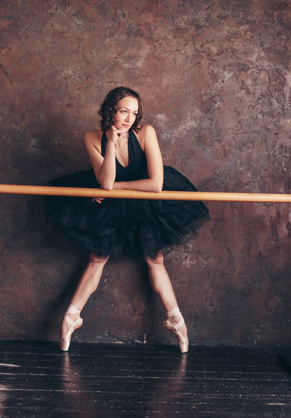 Танцовщица балета балерина в красивом черном платье в пачке юбки позирует в лофт-студии
 - Фото, изображение