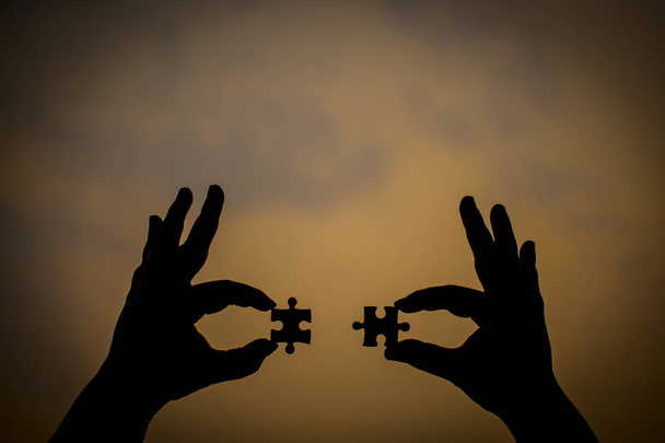 Silhouette of a hand holding a jigsaw puzzle piece isolated with - Photo, Image