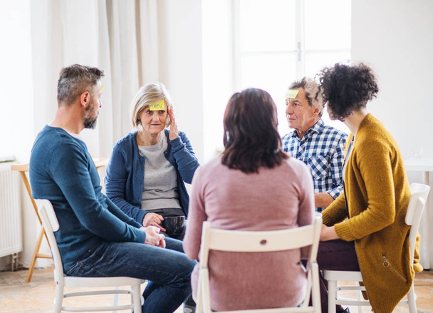 Men and women sitting in a circle during group therapy, adhesive notes on forehead. - Photo, Image