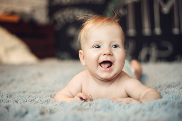 charming baby of 6 months is lying on his stomach on a bed in a bright real interior, with the end of childhood and healthy development - Zdjęcie, obraz
