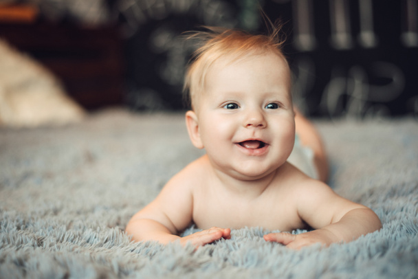 charming baby of 6 months is lying on his stomach on a bed in a bright real interior, with the end of childhood and healthy development - Foto, afbeelding