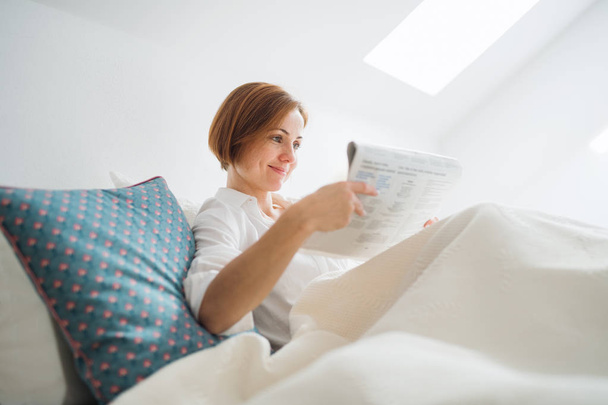 A young woman reading newspapers in bed in the morning in a bedroom. - Foto, immagini
