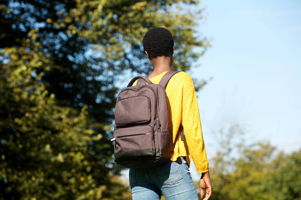 Πορτραίτο από πίσω νεαρή μαύρη γυναίκα το περπάτημα στο πάρκο με τσάντα - Φωτογραφία, εικόνα