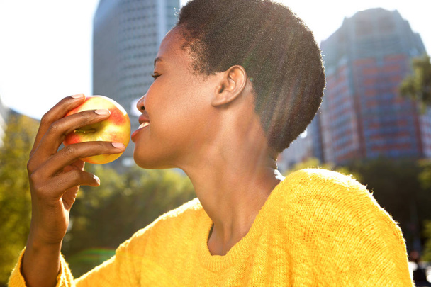Close up side portrait of healthy young black woman with apple outdoors - 写真・画像