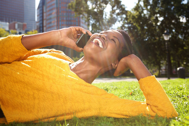 Portrait of happy young african american woman relaxing in park and talking with cellphone  - Photo, Image
