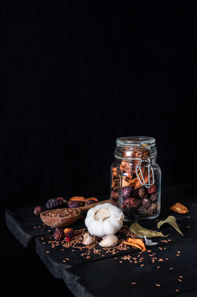 Σκόρδο, ξηρούς καρπούς και τους σπόρους σε σκούρο φόντο για ρουστίκ. Καλλιτεχνική φωτογραφία από σκόρδο και ξηρά φρούτα σε ένα βάζο στο παλιό μαύρο πίνακα πυροβόλησε στο χαμηλό βασικό chiaroscuro στυλ - Φωτογραφία, εικόνα