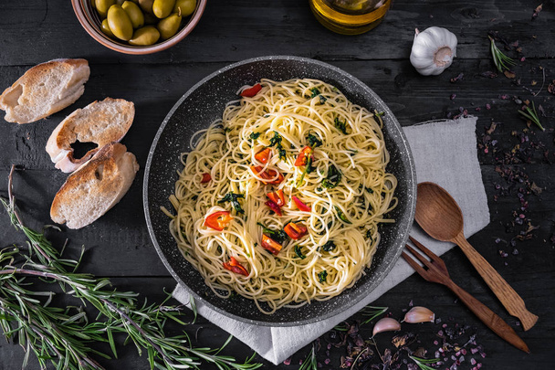 Pan of cooked italian pasta, top view. Flat lay of traditional spaghetti meal with vegetables, garlic and olives on black rustic background - Photo, image