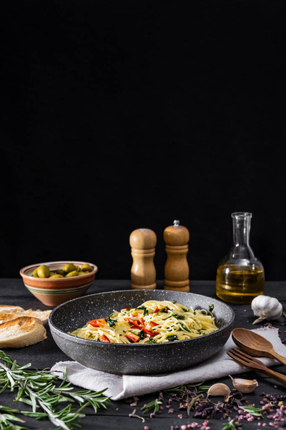 Pan of cooked italian pasta, copy space. Traditional spaghetti meal with vegetables and olives on black rustic background - Valokuva, kuva