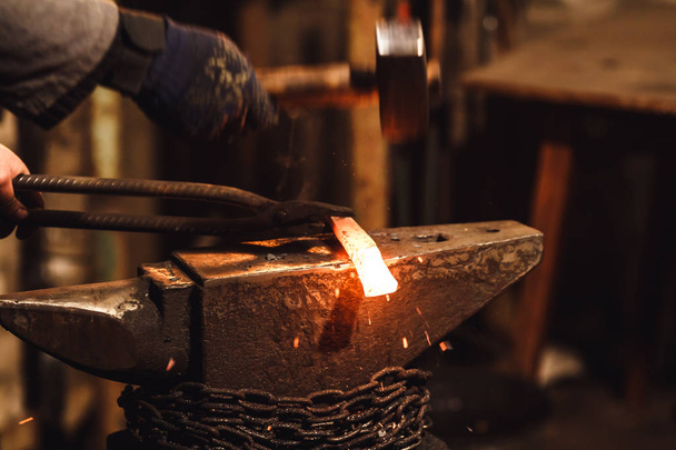 El herrero forja manualmente el metal al rojo vivo en el yunque en la herrería con fuegos artificiales de chispa
. - Foto, Imagen