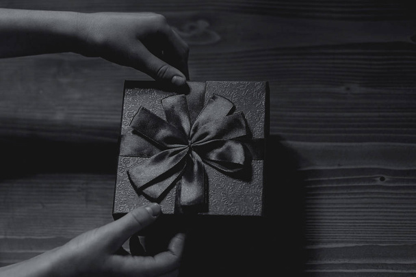 развязать бантик на подарочной коробке на деревянном фоне, вид сверху. black-white
 - Фото, изображение