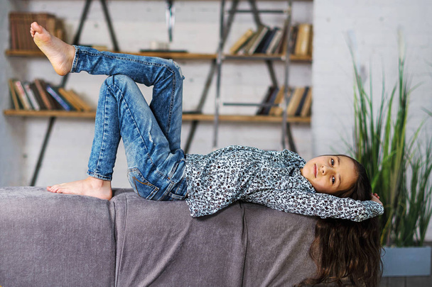 Mladá klidná dospívající dívka s dlouhými vlasy, ležící na zádech na pohodlné pohovce, ruce uvolněné za hlavou. - Fotografie, Obrázek