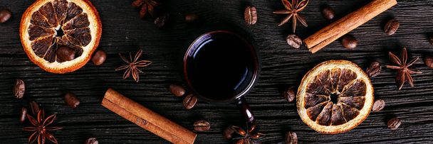 A cup of coffee, star anise, cinnamon, dried orange and coffee beans on a dark kitchen countertop. Fragrant spices for drink, close-up, top view, flat ley. - Zdjęcie, obraz