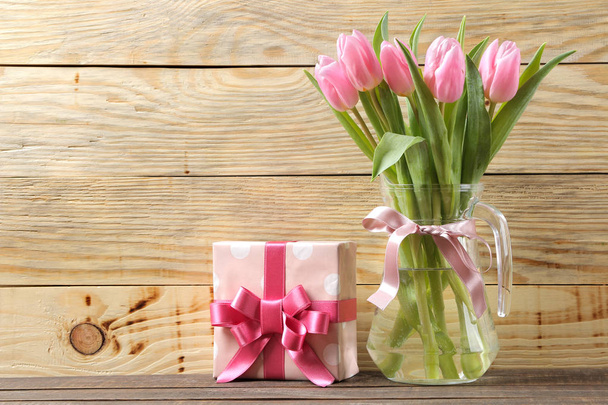 Beautiful bouquet of pink tulips flowers in a vase and gift box on a natural wooden background. place for text. Spring. holidays. - 写真・画像