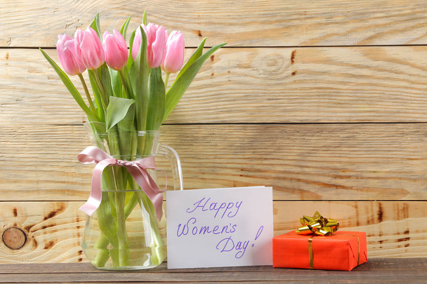 Beautiful bouquet of pink tulips flowers in a vase and a gift box and the text of a happy women's day on a natural wooden background. place for text. Spring. holidays. - 写真・画像