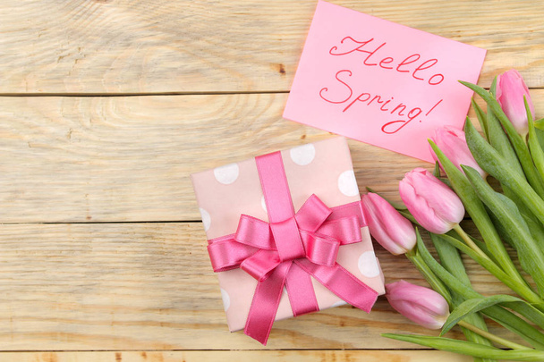 Beautiful bouquet of pink tulips flowers, gift box and text hello spring on paper on a natural wooden background. view from above. Spring. holidays. - Fotoğraf, Görsel