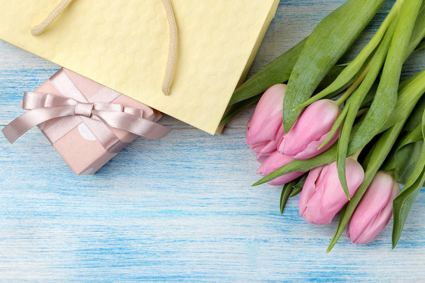 Beautiful bouquet of pink tulips flowers and package with gift box on the blue wooden background. top view. Spring. holidays. - Фото, изображение