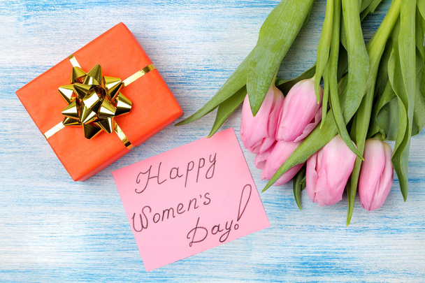 schöner Strauß rosa Tulpenblüten, Geschenkbox und Text glücklicher Frauentag auf Papier auf blauem Holzgrund. Blick von oben. Frühling. Urlaub. - Foto, Bild