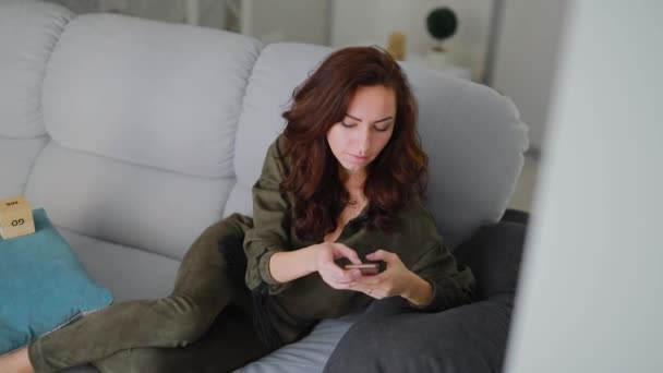 Beautiful woman use her smartphone sitting on sofa at home - Felvétel, videó
