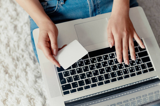 Γυναίκα κρατώντας online shoping, πληρωμή, πιστωτική κάρτα, και να εργάζονται σε ένα φορητό υπολογιστή θηλυκό χρησιμοποιώντας ένα φορητό υπολογιστή που κάθονται στο πάτωμα, ψάχνοντας web, πληροφορίες περιήγησης, έχοντας χώρο εργασίας στο σπίτι. Έννοια του blogging. Σύγχρονες τεχνολογίες. Το top view. - Φωτογραφία, εικόνα