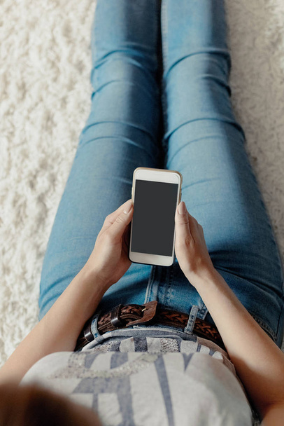 Young woman holding credit card and using phone sitting on floor. Payment.  Online shopping concept.Concept of blogging. Modern technologies Top view. - 写真・画像