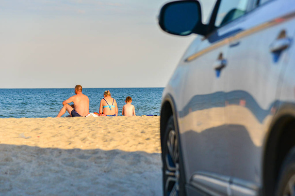 Młoda rodzina z dzieckiem siedzi na plaży na tle samochodów - Zdjęcie, obraz
