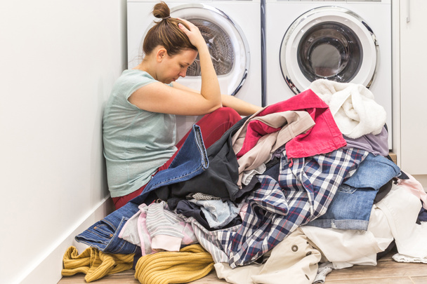 Zdenerwowana Kobieta w pokoju pranie siedzi ona podłogi z brudne ubrania - Zdjęcie, obraz