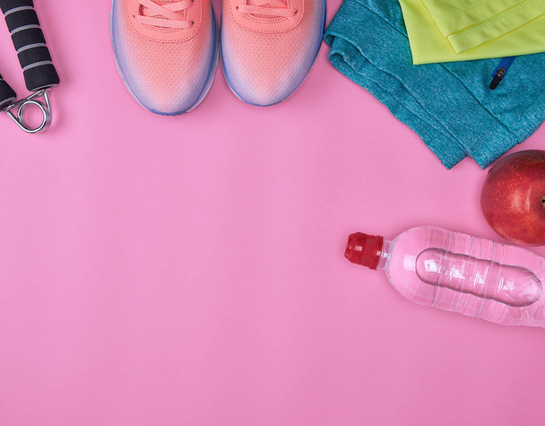 спортивне текстильне взуття та інші предмети для фітнесу на рожевому фоні, вид зверху
 - Фото, зображення