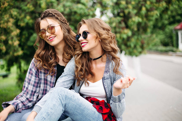 Δυο όμορφα μοντέρνα κορίτσια εφήβων σε γυαλιά ηλίου στο πάρκο. - Φωτογραφία, εικόνα