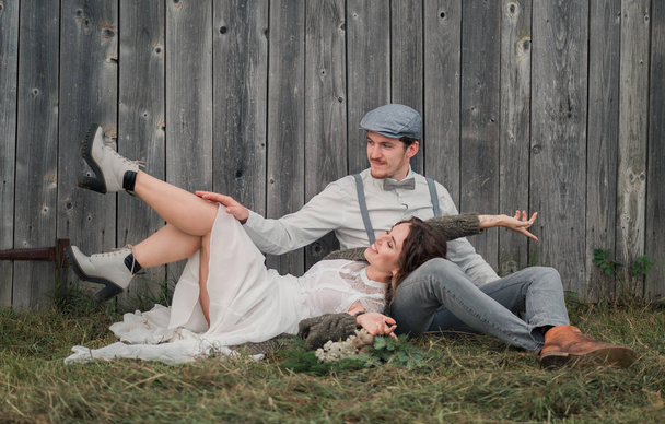 felices recién casados en estilo vaquero sentarse y divertirse, cerca de la pared de madera gris. Hermosa pareja con montañas vista increíble
 - Foto, imagen