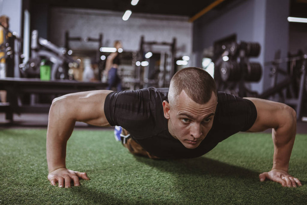 Male athlete doing pushups at the gym, copy space. Young healthy sportsman working out at the gym, doing pushups. Handsome fitness man exercising at sport studio. Lifestyle, activity concept - Zdjęcie, obraz