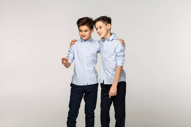 Portrait of two young brothers in blue shirts with short hair, one is pointing right, showing somesing to his brother - Фото, изображение