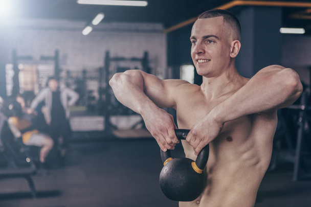 Shirtless handsome muscular man smiling, working out with kettle bell at the gym. Healthy ripped male athlete in functional crossfit training at sports studio, copy space. Health, active lifestyle concept - Fotografie, Obrázek
