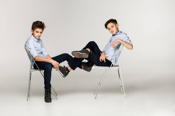 Two boys teenagers in blue shirts sitting on chairs - Fotó, kép