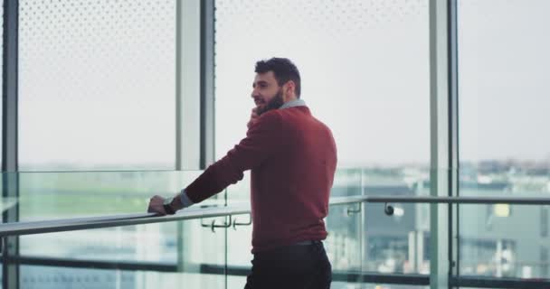 Businessman have a conversation on his smartphone in the airport , he are in a good mood , standing beside of a big window view. - Imágenes, Vídeo