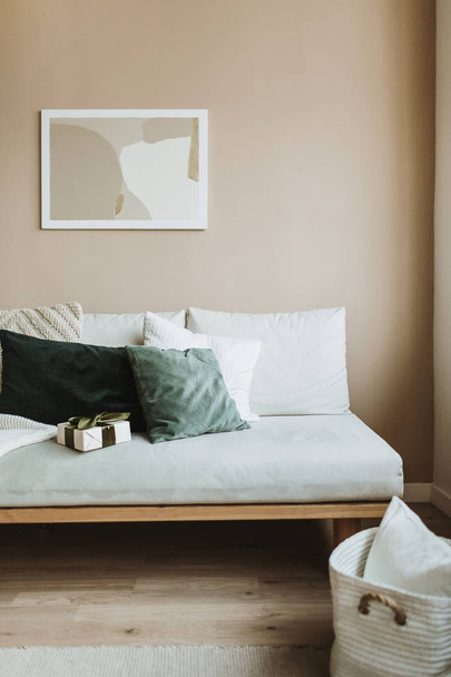 Moderni sisustuskonsepti. Minimaalinen pohjoismainen skandinaavinen olohuone valokuvakehys pastelli beige seinälle, sohva tyynyt ja lahjapaketti. Mukava huoneisto vuokrattavana
. - Valokuva, kuva