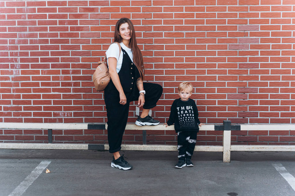 Μητέρα και ο μικρός γιος θέτοντας σε τούβλο τοίχο φόντο - Φωτογραφία, εικόνα