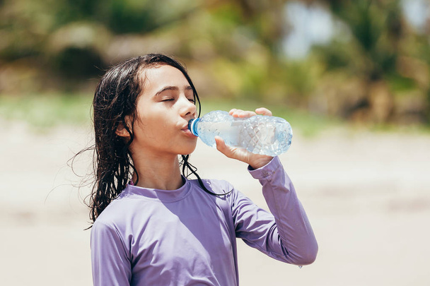 Portrait of little girl drinking water on the beach - Фото, изображение
