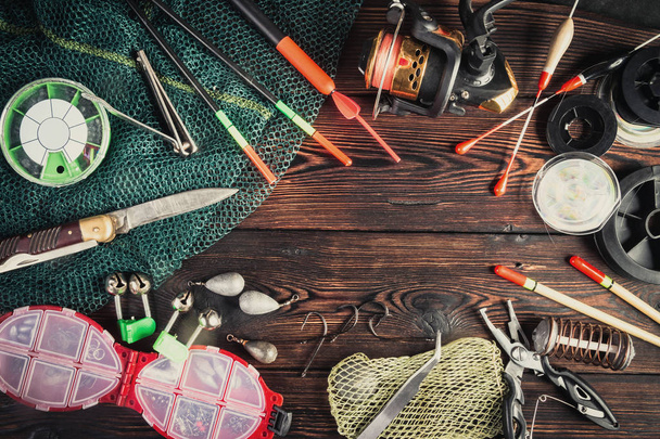 Fishing tackle - fishing, hooks, fishing line and floats, fishing rod with a reel, net, knife and other tools on a wooden background. Still life. View from above. - Foto, Bild