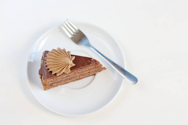 Ένα κομμάτι νόστιμο κέικ σοκολάτας με κρέμα διακόσμηση σοκολάτας σε ένα λευκό πιάτο με επιδόρπιο πιρούνι το top view. Στυλ του μενού - Φωτογραφία, εικόνα