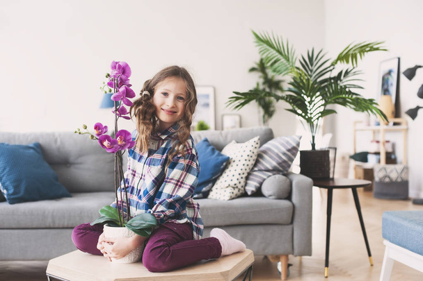 happy kid posing with orchid flower at home. Moving to new apartment concept - 写真・画像