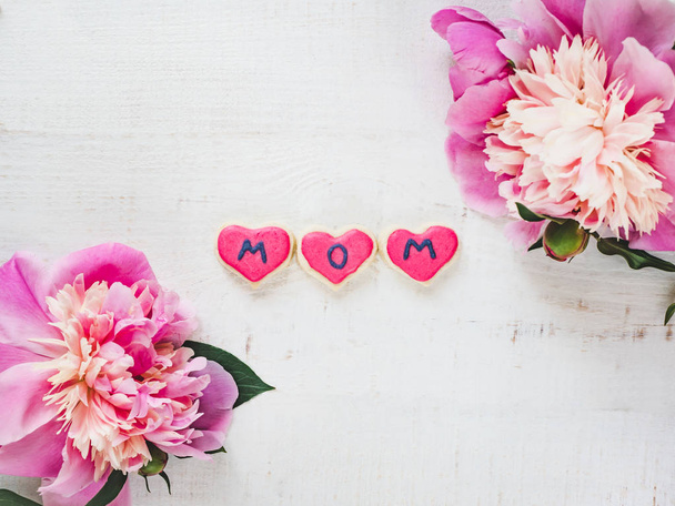 Bright flowers and pink, glazed cookie with the word MOM on a white, isolated background. Top view, close-up. Happy family concept - Fotoğraf, Görsel